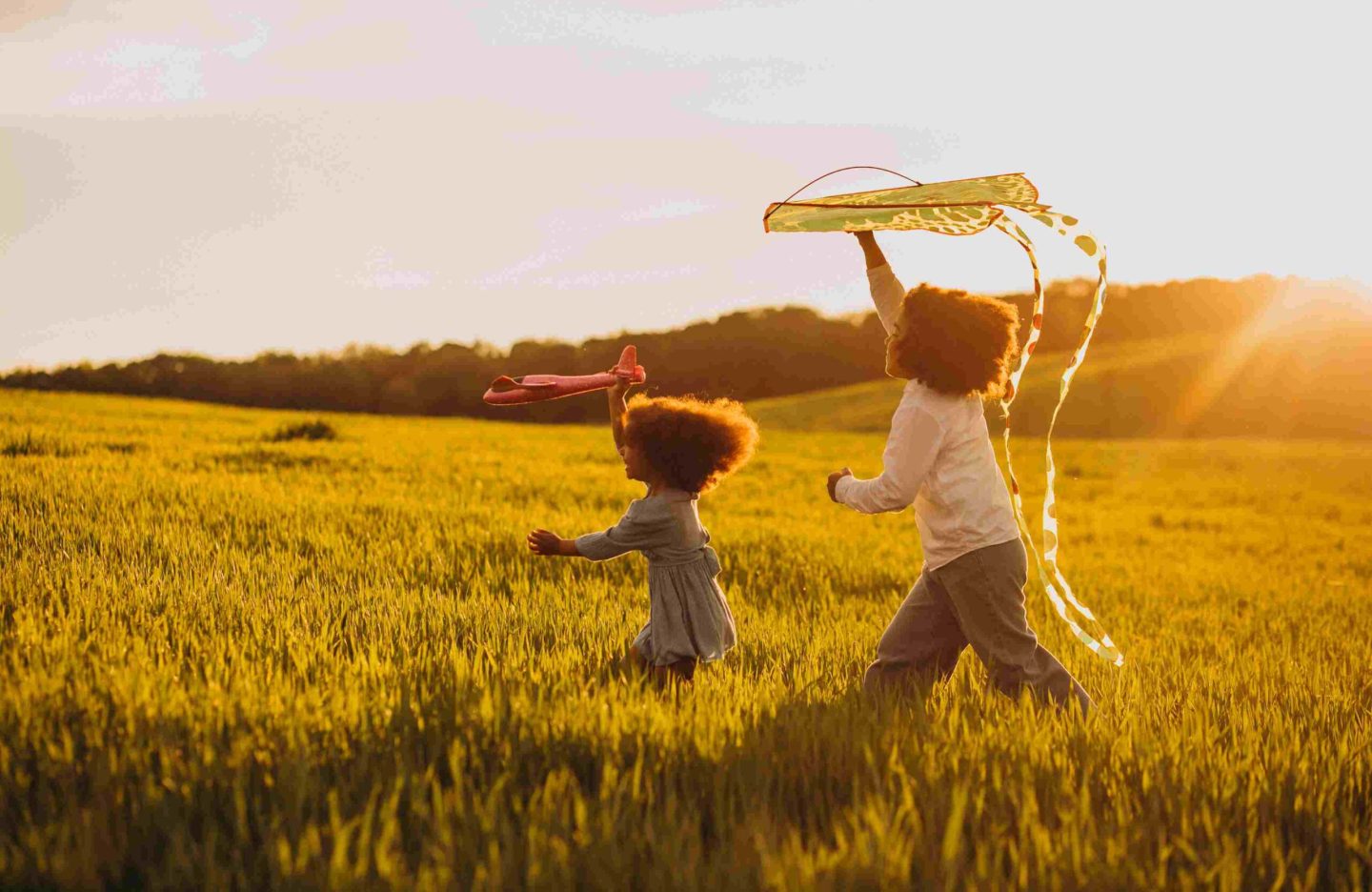 brother-sister-playing-with-kite-plane-field-sunset-1.jpg