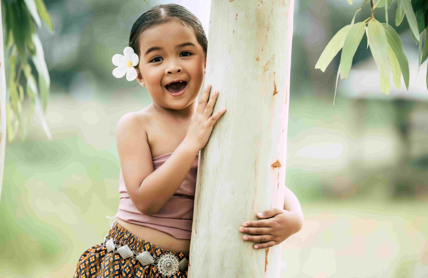 close-up-portrait-little-girl-thai-traditional-dress-put-white-flower-her-ear-stand-embrace-trunk-tree-laugh-copy-space-scaled.jpg